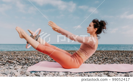 Woman sea pilates. Sporty happy middle aged woman practicing fitness on beach near sea, smiling active female training with ring on yoga mat outside, enjoying healthy lifestyle, harmony and meditation Woman sea pilates. Sporty happy middle aged woman practicing fitness on beach near sea, smiling active female training with ring on yoga mat outside, enjoying healthy lifestyle, harmony and meditation 99052417