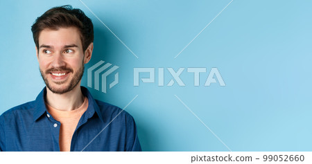 Close up of handsome confident man with beard, looking at empty space and smiling, standing on blue background Close up of handsome confident man with beard, looking at empty space and smiling, standing on blue background 99052660