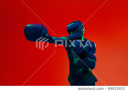 Sporty man wearing head guard and boxing gloves practicing for fight on studio background Sporty man wearing head guard and boxing gloves practicing for fight on studio background 99052852