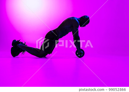 Bodybuilder working on his abs with a ab roller on studio background with color filter Bodybuilder working on his abs with a ab roller on studio background with color filter 99052866