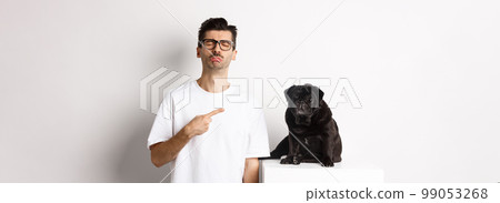 Sad and gloomy pet owner pointing at his black pug dog and sobbing, standing upster against white background Sad and gloomy pet owner pointing at his black pug dog and sobbing, standing upster against white background 99053268