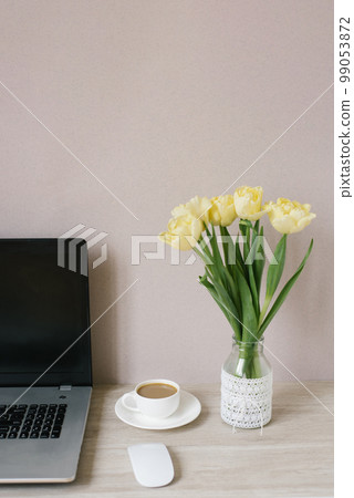 Home office interior. A laptop, a bouquet of yellow tulips in a vase, a cup of coffee. Lunch break at the workplace Home office interior. A laptop, a bouquet of yellow tulips in a vase, a cup of coffee. Lunch break at the workplace 99053872