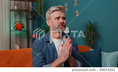 Middle-aged mature old man praying sincerely with folded arms asking God for help, begging apology Middle-aged mature old man praying sincerely with folded arms asking God for help, begging apology 99054261