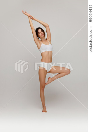 Well-being. Full-length portrait of beautiful young slim girl posing in white underwear posing over grey studio background. Concept of body and skincare, beauty 99054455