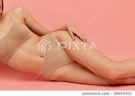 Cropped image of slim smooth female legs, breast and belly over pink studio background. Model posing in underwear. Concept of body and skincare, beauty 99054501