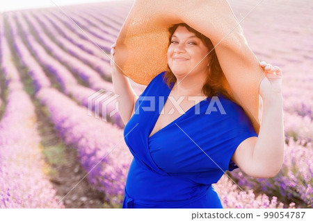 Woman lavender field sunset. Romantic woman walks through the lavender fields. illuminated by sunset sunlight. She is wearing a blue dress with a hat. Woman lavender field sunset. Romantic woman walks through the lavender fields. illuminated by sunset sunlight. She is wearing a blue dress with a hat. 99054787