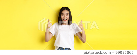 Pretty young asian woman in white t-shirt, showing thumbs up and smiling, praise good offer, recommend product, standing satisfied over yellow background Pretty young asian woman in white t-shirt, showing thumbs up and smiling, praise good offer, recommend product, standing satisfied over yellow background 99055865