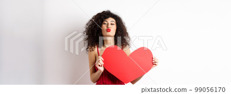 Romantic woman in dress showing big red heart, pucker lips for kiss and express love, express sympathy, white background Romantic woman in dress showing big red heart, pucker lips for kiss and express love, express sympathy, white background 99056170