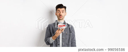Man celebrating birthday, blowing candle on cake and making wish, standing on white background 99056586