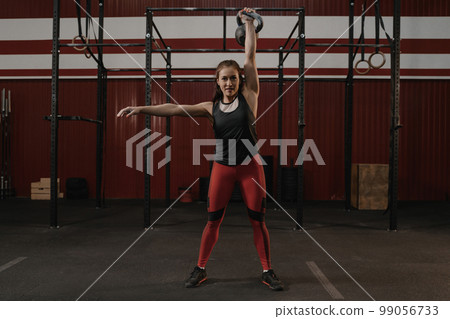 Strong cheerful woman with muscular body exercising with kettlebell while crossfit training. 99056733