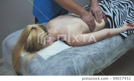 A masseur massages a girl's back. 99057452