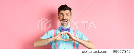 Happy Valentines day. Cheerful male model enjoying romantic date, showing heart sign, say I love you and looking left with happy smile, standing over pink background Happy Valentines day. Cheerful male model enjoying romantic date, showing heart sign, say I love you and looking left with happy smile, standing over pink background 99057542