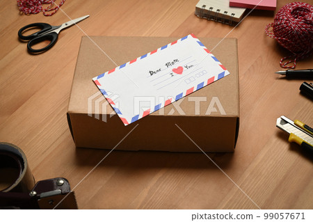 Gift boxes with greeting card surrounded by gift wrapping materials on wooden table 99057671