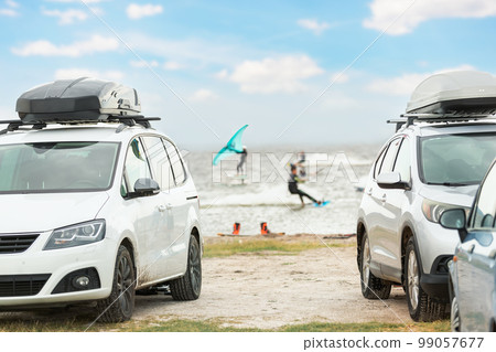 Front view many cars parked with surf board kite equipment on sand beach, van vehicle with rooftop box ocean sea beach watersport spot camp. Adventure travel water sport acitivity 99057677