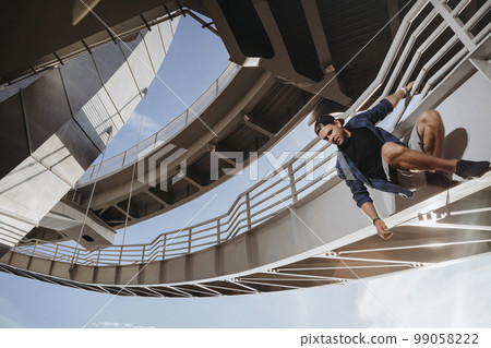 Freerunning athlete is hanging on the bridge and getting ready for a dangerous jump Freerunning athlete is hanging on the bridge and getting ready for a dangerous jump 99058222