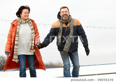 Middle-aged smiling happy people, man and woman spending time on open ice rink in winter day. Concept of leisure activity, winter hobby, relationship, emotions Middle-aged smiling happy people, man and woman spending time on open ice rink in winter day. Concept of leisure activity, winter hobby, relationship, emotions 99059239