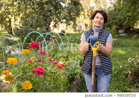 Mature woman standing relaxed near flowers with shovel in backyard smiling 99059550