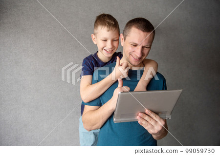 Cute boy hugs dad from behind, talking on a video link in a tablet 99059730