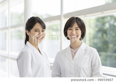 Two young women in white coat looking at camera portrait Two young women in white coat looking at camera portrait 99059987