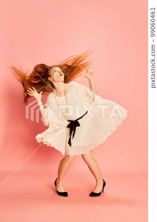 One young beautiful redhaired girl with long hair dancing, posing isolated over light pink background. Concept of positive emotions, happy mood, fashion, youth One young beautiful redhaired girl with long hair dancing, posing isolated over light pink background. Concept of positive emotions, happy mood, fashion, youth 99060461