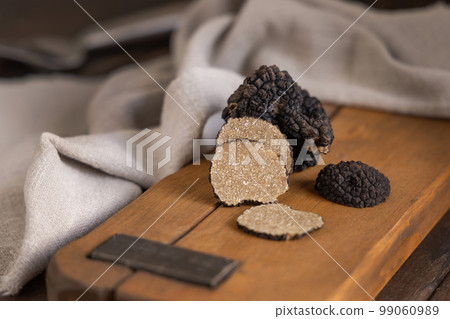 Whole and sliced black truffles mushroom on wooden board on dark brown table, close up 99060989
