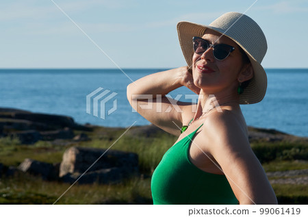 Woman tourist in a straw hat and a green dress on the seashore on a bright sunny day 99061419