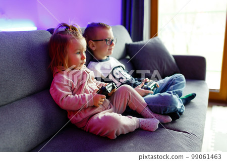 The boy Danya and his younger sister Emilia play on the console. 99061463