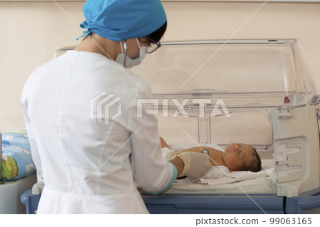 Neonatology. Doctor listening to the heartbeat of a newborn in an infant incubator 99063165