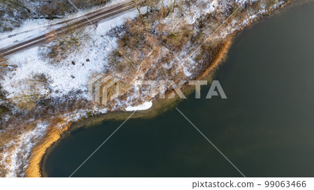 Aerial view of the winter snow covered forest and frozen lake from above captured with a drone. High Aerial view of the winter snow covered forest and frozen lake from above captured with a drone. High 99063466