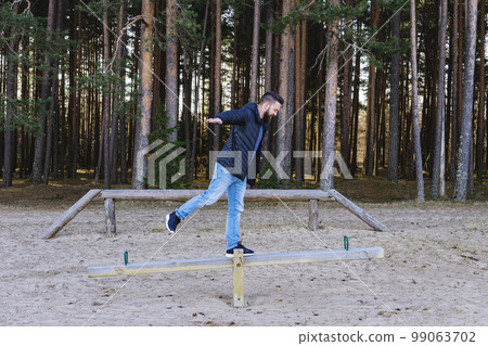 Adult bearded man hipster staying on swing at a play area in the forest. Concept of sanity, harmony and balance Adult bearded man hipster staying on swing at a play area in the forest. Concept of sanity, harmony and balance 99063702