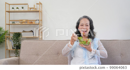 Happy old woman eating healthy vegetable salad at home 99064063