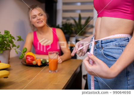woman measures her waist with measure tape in the company of a friend woman measures her waist with measure tape in the company of a friend 99064698