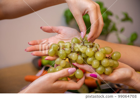 Close-up on the hands of two women handing each other a bunch of grapes Close-up on the hands of two women handing each other a bunch of grapes 99064708