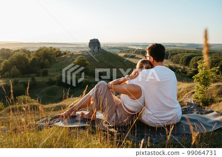 Man and Woman Enjoying Picnic with Beautiful Sunset Outdoors, Scenic Landscape and Nature Miracle Giant Stone on the Background Man and Woman Enjoying Picnic with Beautiful Sunset Outdoors, Scenic Landscape and Nature Miracle Giant Stone on the Background 99064731