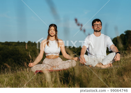 Young Adult Couple Meditating Outdoors, Caucasian Woman and Man Dressed Alike Breathing Fresh Air in the Nature Young Adult Couple Meditating Outdoors, Caucasian Woman and Man Dressed Alike Breathing Fresh Air in the Nature 99064746
