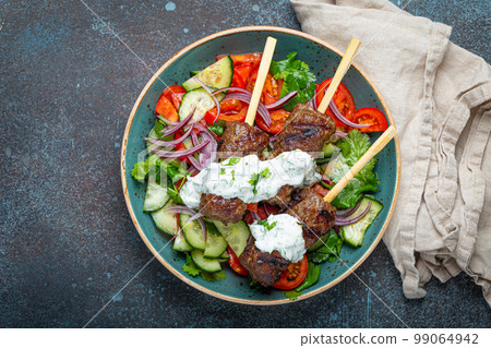 Grilled skewer meat beef kebabs on sticks served with fresh vegetables salad on plate on rustic concrete background from above. Traditional Middle Eastern, Turkish dish Kebab 99064942