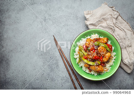 Asian sweet and sour sticky chicken with vegetables stir-fry and rice in ceramic bowl with chopsticks top view on gray rustic stone background, traditional Asian dish. Copy space 99064968
