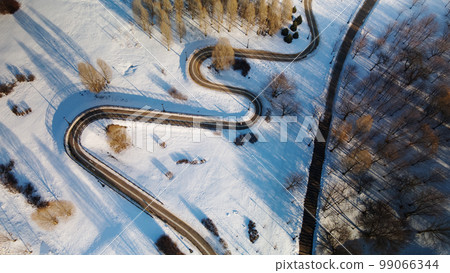 A winding bike path in a city park. City park in winter. Snow lies on the ground. Aerial photography. A winding bike path in a city park. City park in winter. Snow lies on the ground. Aerial photography. 99066344