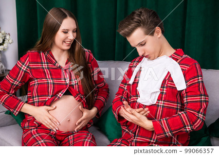 A man and a pregnant woman with an exposed belly sit on a couch. A man and a pregnant woman with an exposed belly sit on a couch. 99066357
