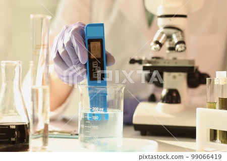 Scientist in latex gloves measures characteristics of aqueous solution in laboratory glassware. Scientist in latex gloves measures characteristics of aqueous solution in laboratory glassware. 99066419