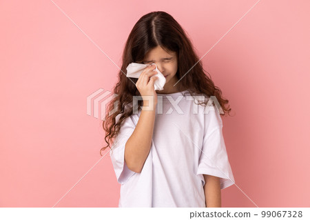 Portrait of sad upset unhappy little girl wearing white T-shirt crying, hard going through loss or defeat, feeling sorrow, holding handkerchief. Indoor studio shot isolated on pink background. 99067328