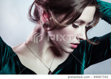 Beauty portrait of very beautiful woman with natural makeup wearing green dress posing with raised arms, looking down, being attractive and gently. Indoor studio shot isolated on gray background. 99067392
