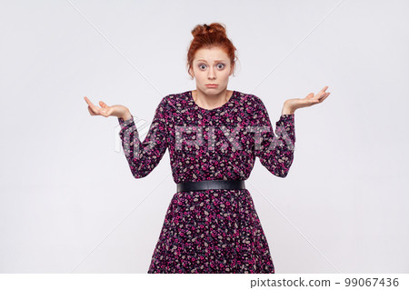 Maybe, don't know. Unsure uncertain redhead woman wearing dress raising hands with confused perplexed puzzled expression, not sure about decision. Indoor studio shot isolated on gray background. 99067436