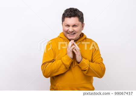 Cunning middle aged man clasping hands and planning evil tricky prank or scheming, cheating with sly smile, wearing urban style hoodie. Indoor studio shot isolated on white background. 99067437