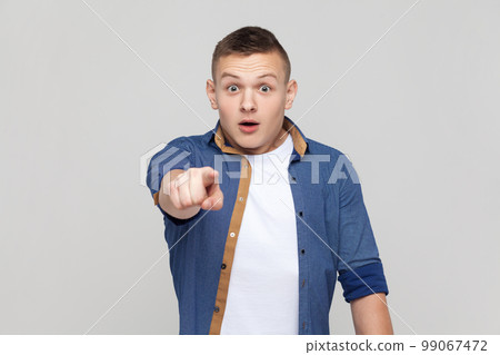 Portrait of astonished amazed handsome teenager boy wearing blue shirt pointing to camera with surprised shocked expression, making choice. Indoor studio shot isolated on gray background. 99067472