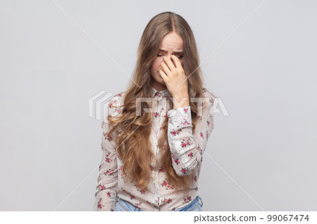 Portrait of desperate depressed woman with wavy blond hair rubbing eyes, crying because of hopelessness and loneliness, nervous breakdown. Indoor studio shot isolated on gray background. 99067474
