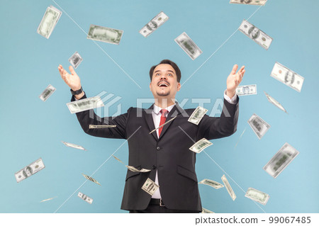 Oh my god, wow. Portrait of man with mustache absolutely shocked of money rain falling from up, rejoicing, wearing black suit with red tie. Indoor studio shot isolated on light blue background. Oh my god, wow. Portrait of man with mustache absolutely shocked of money rain falling from up, rejoicing, wearing black suit with red tie. Indoor studio shot isolated on light blue background. 99067485