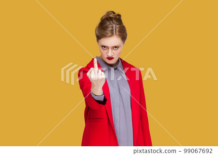Portrait of aggressive rude woman with red lips standing showing middle finger to camera, arguing with somebody, wearing red jacket. Indoor studio shot isolated on yellow background. Portrait of aggressive rude woman with red lips standing showing middle finger to camera, arguing with somebody, wearing red jacket. Indoor studio shot isolated on yellow background. 99067692