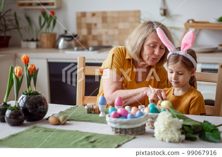Happy easter family elderly grandmother and little granddaughter with rabbit ears are preparing for the holiday to paint eggs 99067916