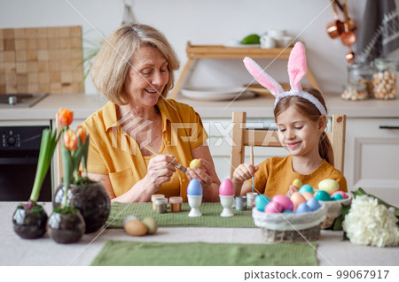 Happy easter family elderly grandmother and little granddaughter with rabbit ears are preparing for the holiday to paint eggs 99067917